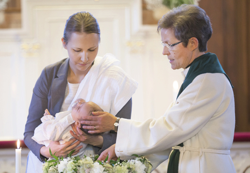 Pappi kastaa lasta kirkossa. Lapsi äidin sylissä.